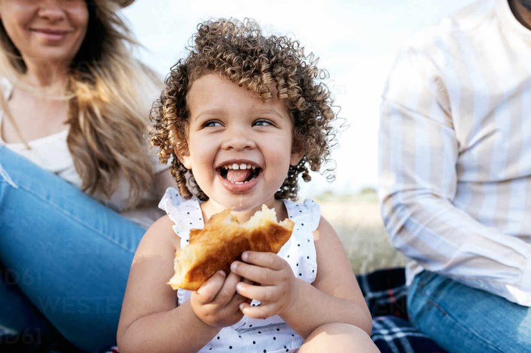 cheerful-little-girl-eating-pastry-looking-away-sitting-with-multiracial-family-enjoying-picnic-together-in-nature-ADSF28353.jpg